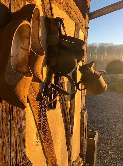 Sabot-normands Détail d’un mur à colombages du Domaine de la Ferme de Fourges, avec sabots normands et accessoires anciens au soleil couchant