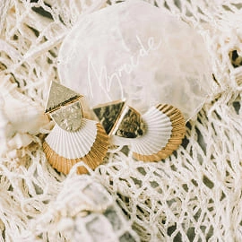 Boucles d’oreilles dorées posées sur une dentelle avec le mot "bride"