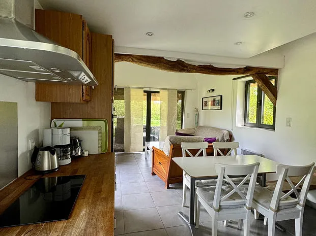 Intérieur lumineux de La Chaumière avec cuisine équipée, coin repas et lit dans une pièce à vivre cosy et ouverte sur le jardin